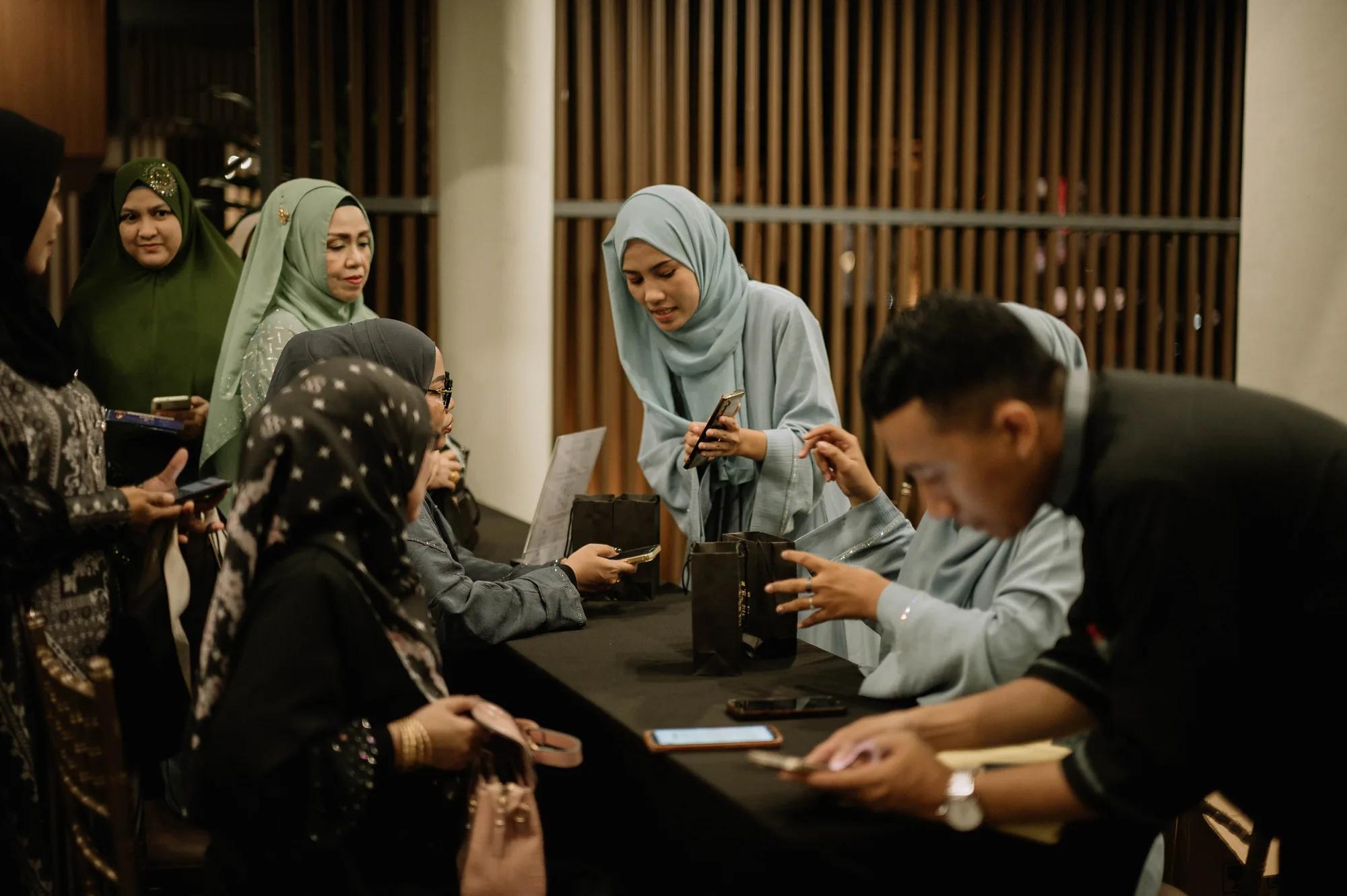 Tim melayani pengunjung di meja acara Heelwa, dengan perangkat digital dan tas belanja di atas meja